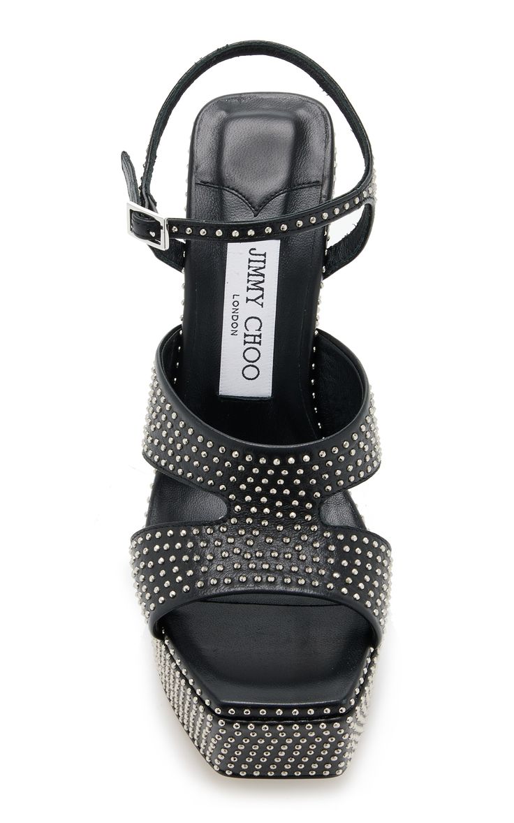 a closeup shot of a pair of black jimmy choo studded platform sandals. the sandals are made of black leather and are adorned with silver studs. the jimmy choo london label is visible on the insole. the shoes are presented on a white background, showcasing their design and details.
