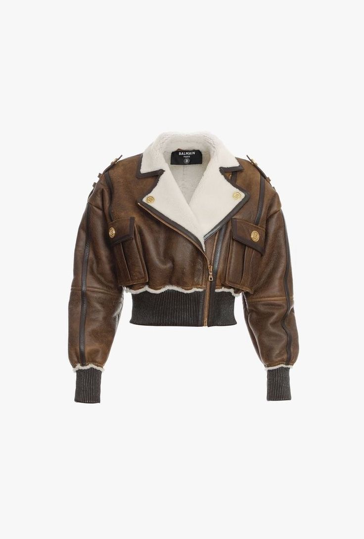 a studio shot of a balmain brown leather jacket with a shearling collar. the jacket is cropped and features gold buttons, pockets, and a ribbed knit cuff. it's a women's jacket, ideal for autumn/winter fashion.  the brand label is visible on the inner collar.