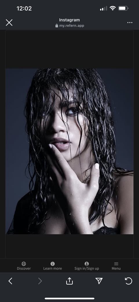 a portrait of a woman with wet, dark hair. she is touching her face with her hand and has a sultry expression. the background is dark, and there are water droplets on her skin and hair. the image appears to be screenshot from a mobile phone screen, including interface elements from instagram and a website called "my.refern.app."