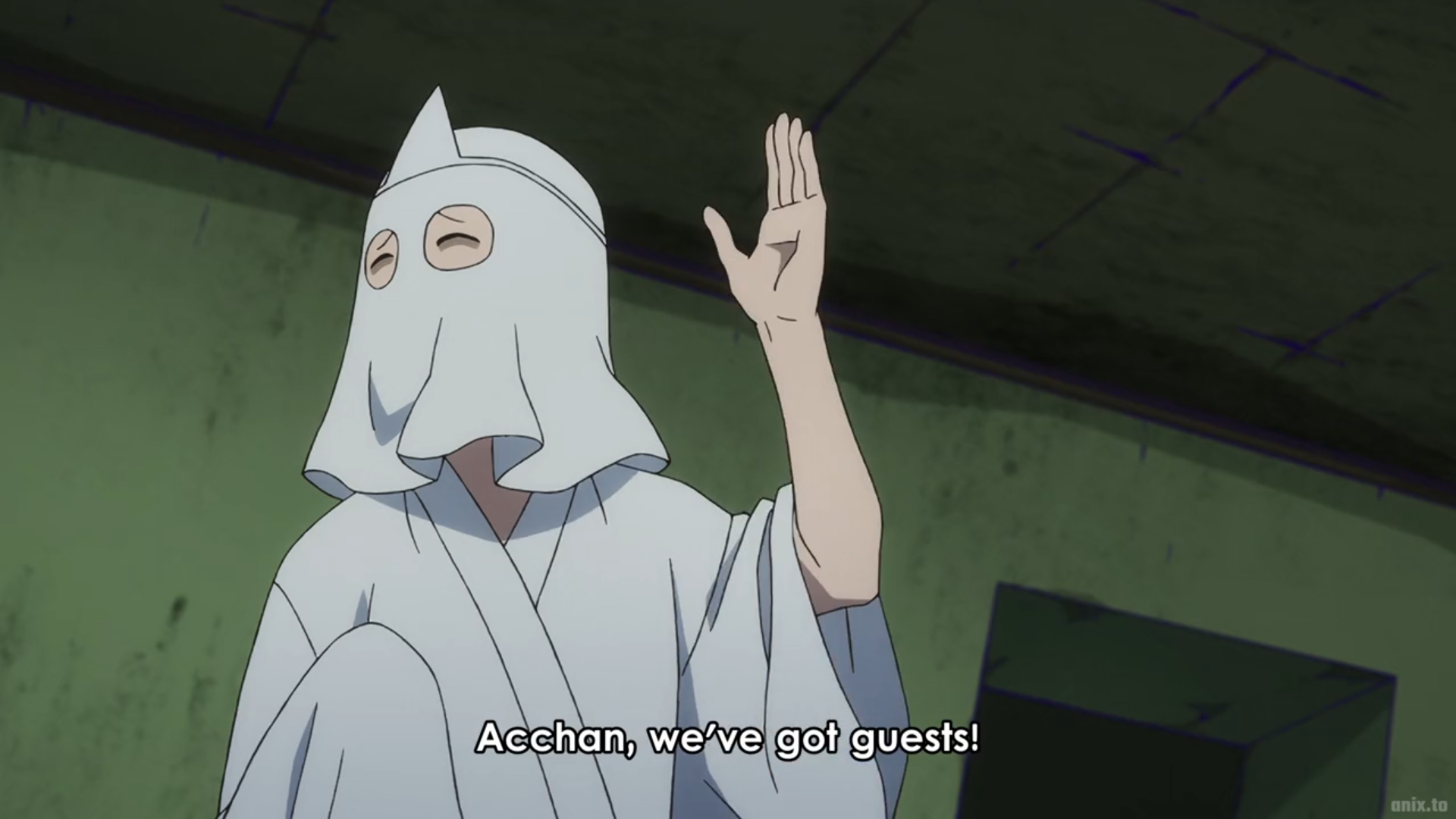 an anime character, a woman wearing a white robe and mask, is waving her hand and smiling as she speaks to someone offscreen. she says "acchan, we've got guests!". the scene takes place in a dark and dirty room with a green and blue background.