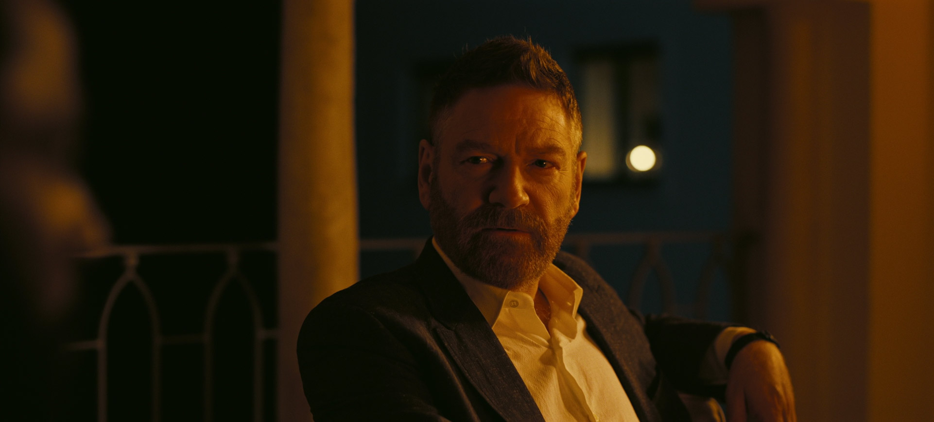 a portrait of a man with a beard and mustache. he is wearing a dark blazer and a white shirt. the background is dark, and the man is lit by warm, artificial light. he has a serious and contemplative expression on his face.  the overall mood of the image is dramatic and intense.