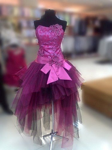 a pink strapless dress with a sequined bodice, ribbon waist, and asymmetrical tulle skirt is displayed on a mannequin.