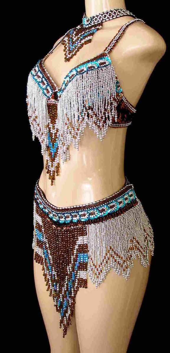 a mannequin wears a twopiece dress, choker necklace, and jewelry made of beads in various shapes and colors. the mannequin has fair skin and a neutral expression. the dress consists of a beaded top and skirt with a fringe. the beads on the clothing are brown, white, and turquoise. the background is black.