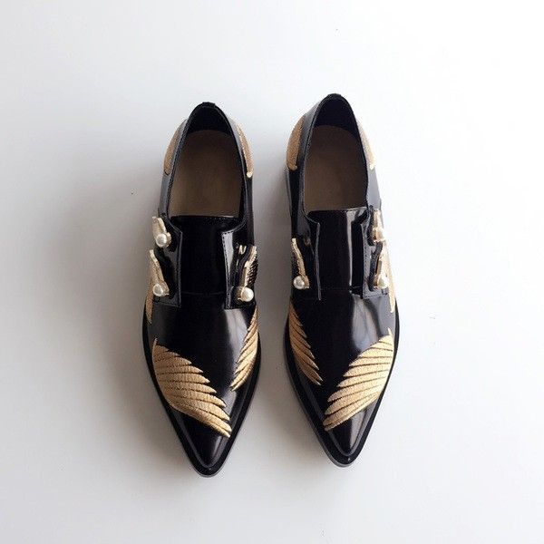 the image shows a pair of women's black leather shoes with gold embroidery in the shape of wings on the sides. the shoes have a pointed toe and slipon design, and they're embellished with small pearl accents near the closure. they are positioned on a white background. the overall style is elegant and sophisticated.