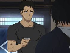two men, one with short black hair and a black shirt and the other with short black hair and a dark blue shirt, are in a dimly lit room. the man in the black shirt is looking at the other man with a serious expression on his face. he is holding a small, white object in his right hand. the other man is looking at the object. the room has wooden walls and a window in the back.