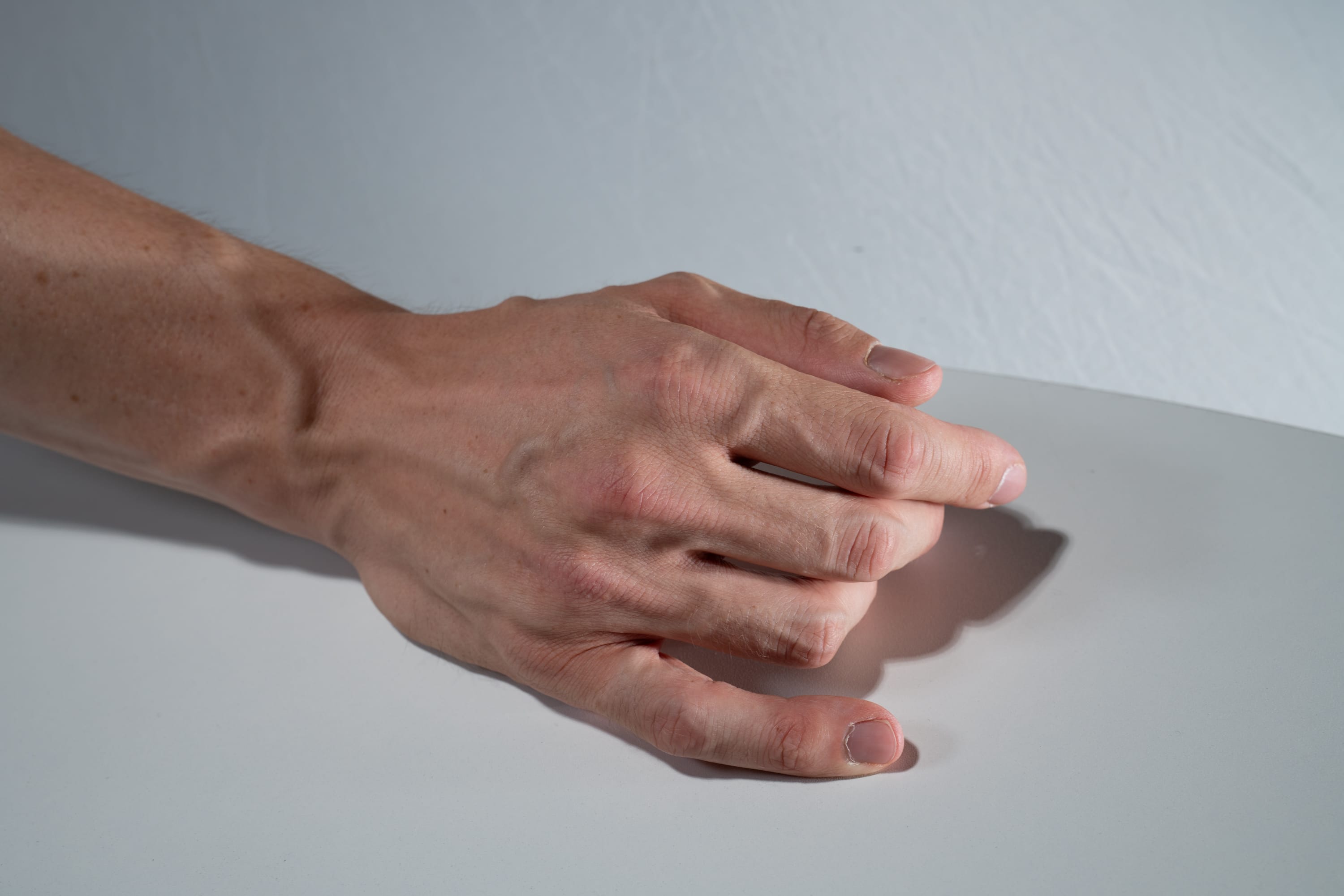 a closeup shot of a fairskinned hand resting on a white surface. the hand is slightly clenched, and the veins on the back of the hand are visible. the lighting is soft and diffused, creating subtle shadows on the surface.