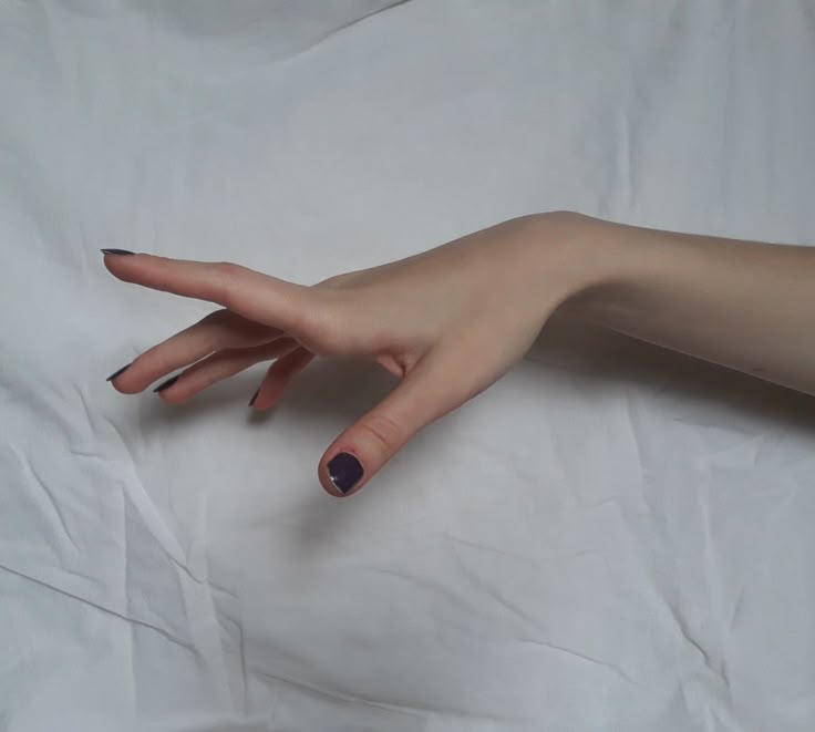 an arm and hand with purple nail polish resting on a white wrinkled background. the hand is outstretched with fingers extended.