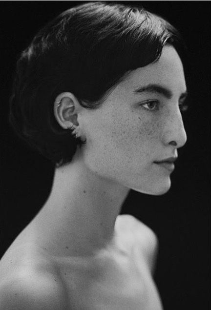 a black and white portrait of a woman in profile, showcasing her freckled face, short hair, ear piercing, neck, and bare shoulder.