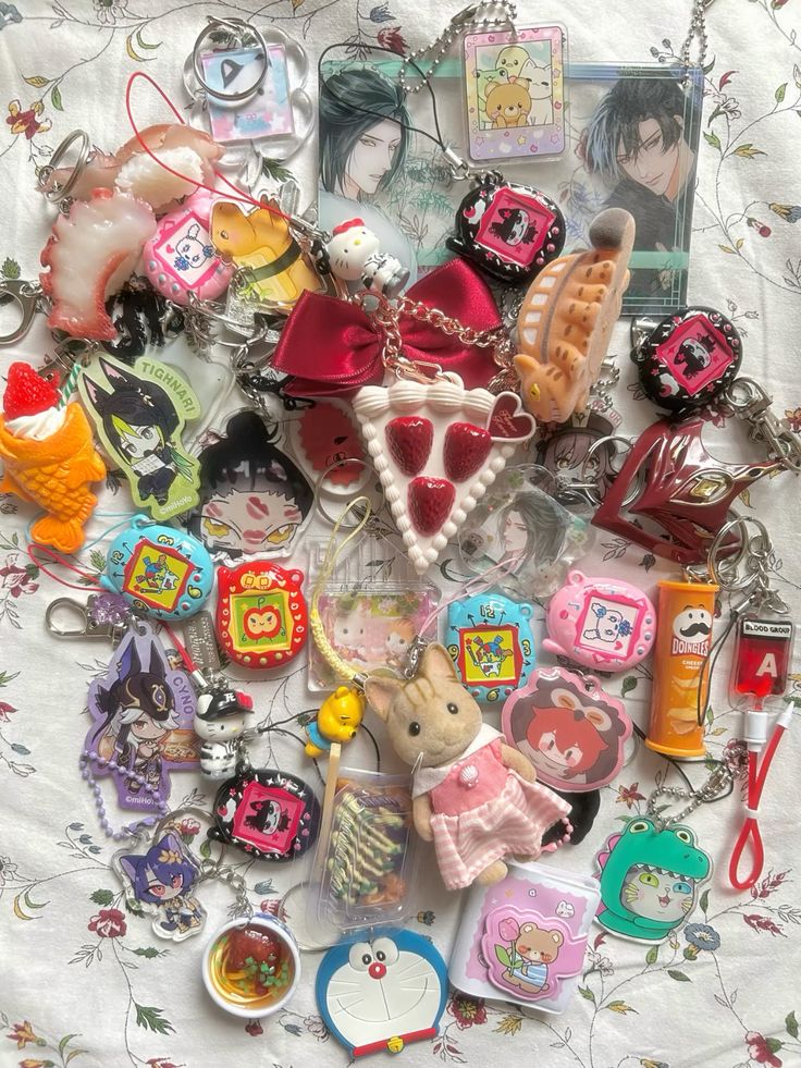 a collection of keychains are displayed on a floral patterned surface. the keychains feature a variety of designs including food items like sushi, doughnuts, and cake, popular cartoon characters such as doraemon and sanrio characters, and animal characters like sylvanian families and tamagotchi. there are also acrylic and enamel keychains with anime and game characters. the collection is colorful and diverse, showcasing a range of interests and themes.