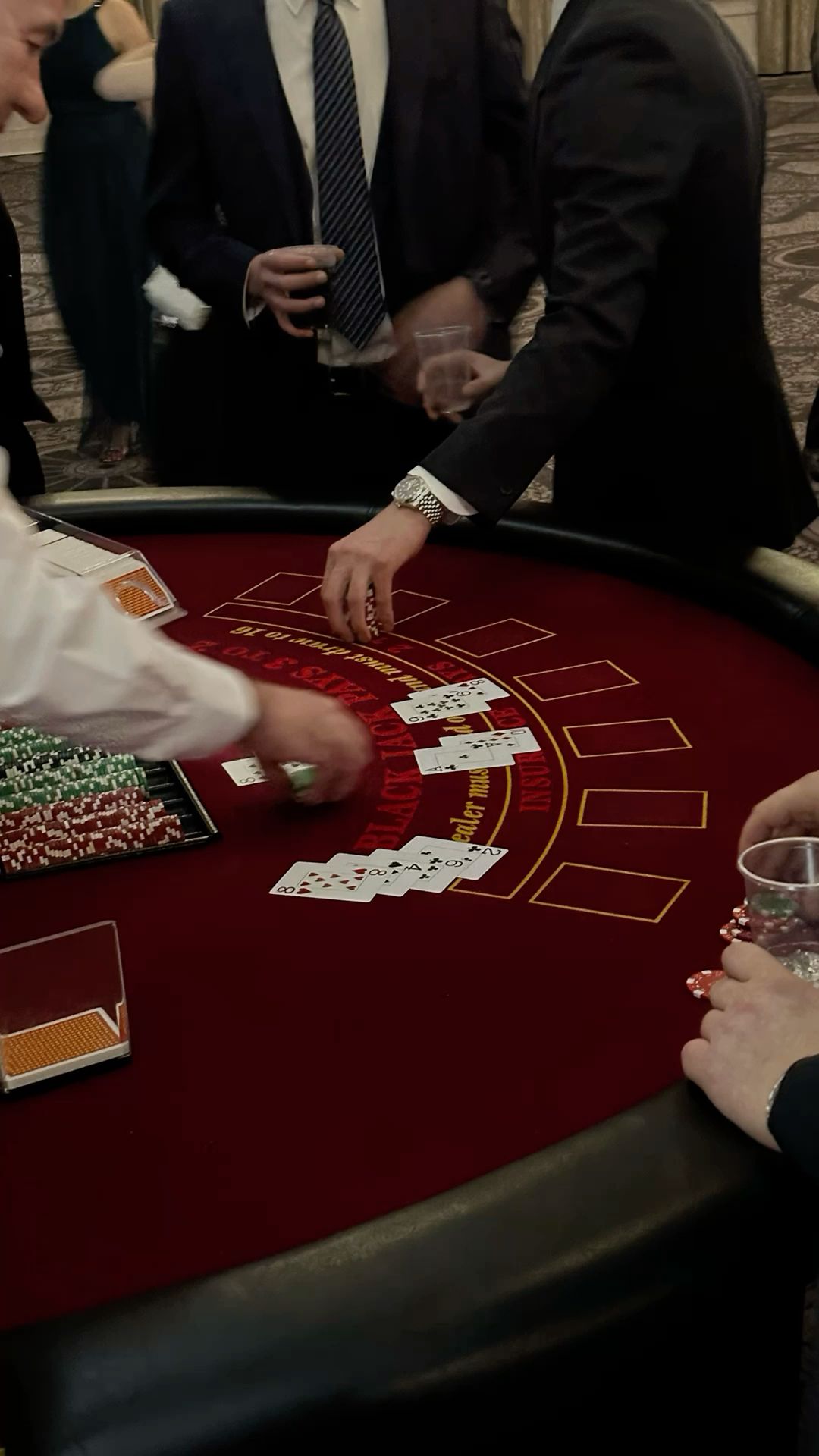 a photo taken from above of a blackjack table, where several people in suits are gathered around it playing a game. there are cards and chips scattered across the table.  the men appear to be enjoying themselves, as they are smiling and laughing. the scene is set in a casino.