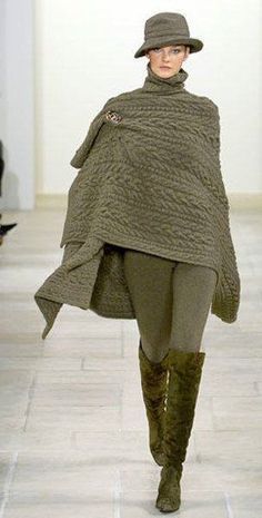 a female model wearing a green poncho, hat, and thighhigh boots. she is walking on a white tiled floor.