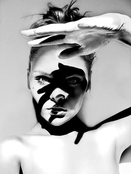 a black and white photo of a woman with her hand raised over her face, creating a shadow that covers most of her face. the photo is shot in a soft, diffused