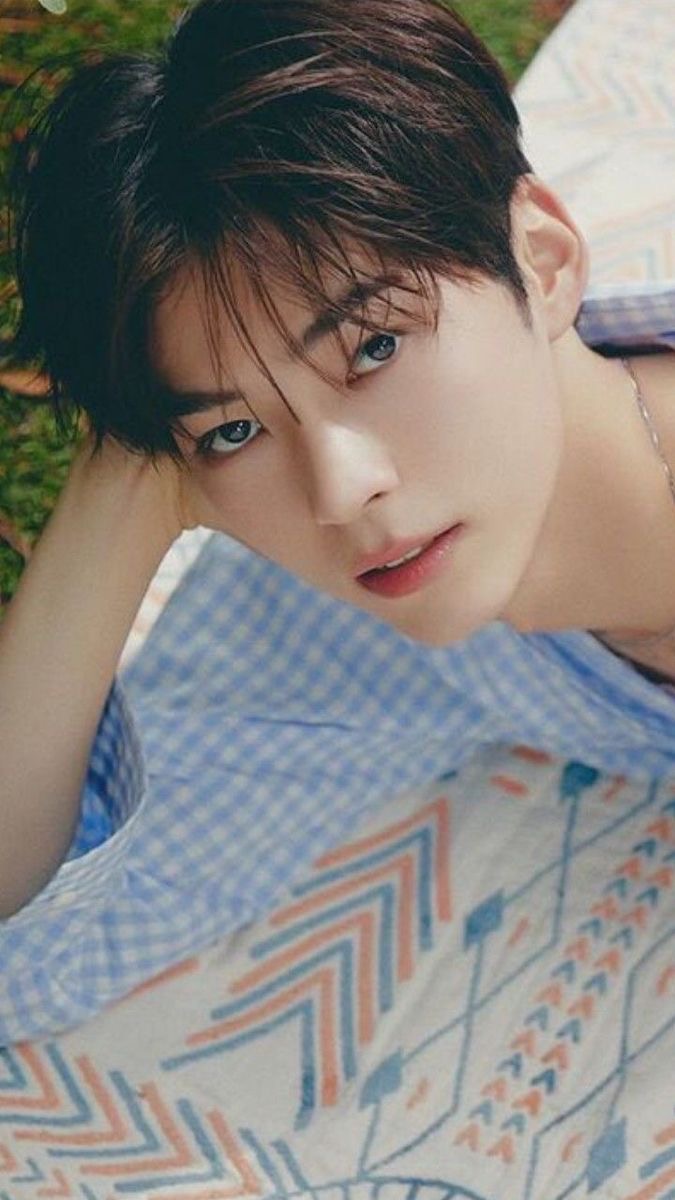 a closeup portrait of a young asian man with dark hair and brown eyes. he is wearing a light blue and white patterned shirt and is lying down. the image has soft lighting and a warm tone.