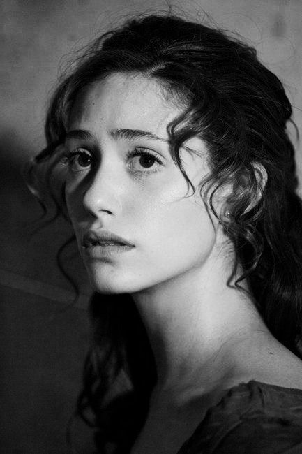 the image is a black and white closeup portrait of a young woman with dark, curly hair. she is looking directly at the camera with a serious, almost melancholic expression.  the lighting is dramatic, with shadows accentuating her features.  her hair is styled in loose curls framing her face. she is wearing a darkcolored top, and a small earring is visible in her ear. the overall mood is contemplative and artistic.