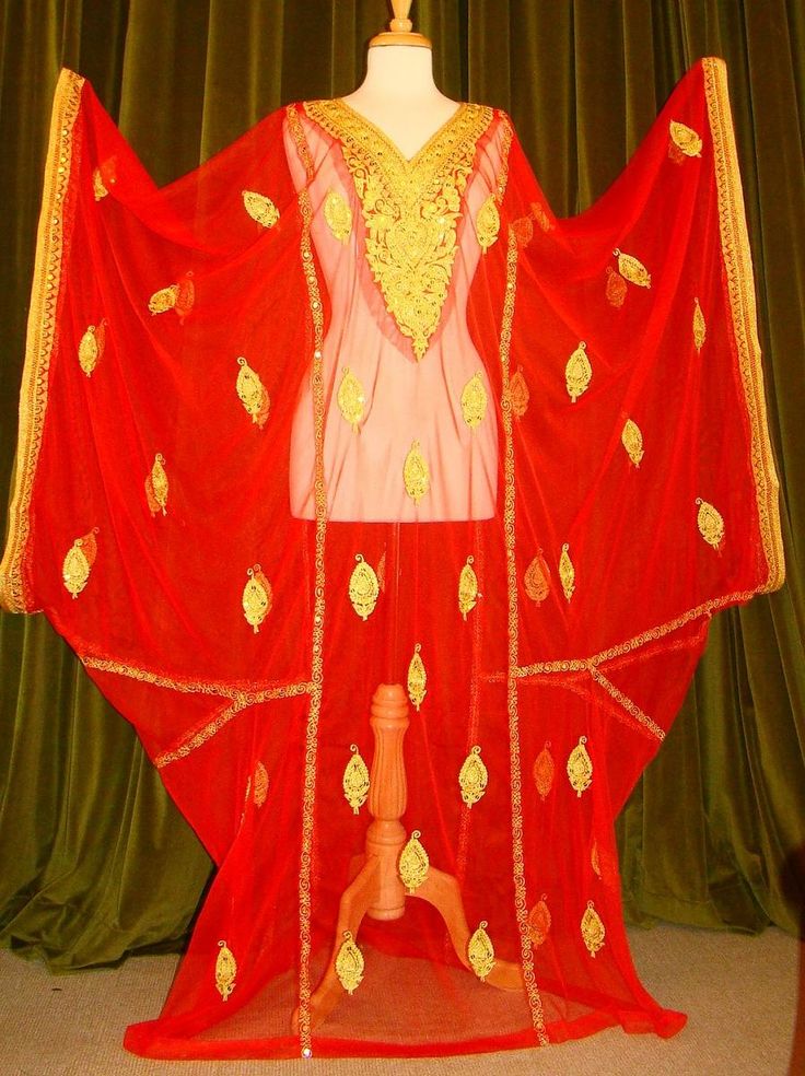 a red caftan with gold embroidery is displayed on a mannequin in front of a green curtain. the caftan is lightweight and flowing, with a vneck and wide sleeves. it is decorated with a repeating pattern of gold teardropshaped motifs.