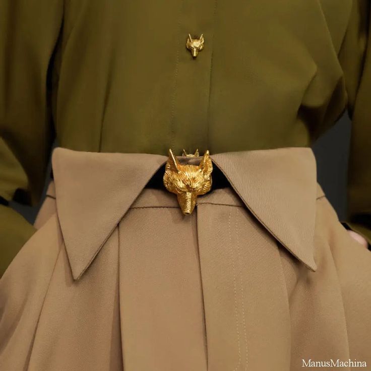 a closeup shot of a woman wearing a stylish outfit. she is wearing a green khaki shirt with a gold fox button and a matching pair of khaki pants. the pants have a gold fox belt buckle. the outfit is very chic and modern.