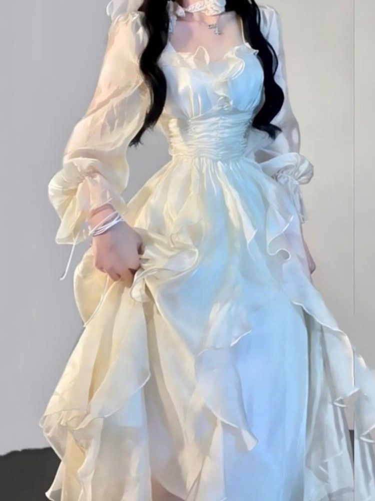 a person wearing a creamcolored ruffled chiffon dress with long, puffy sleeves.