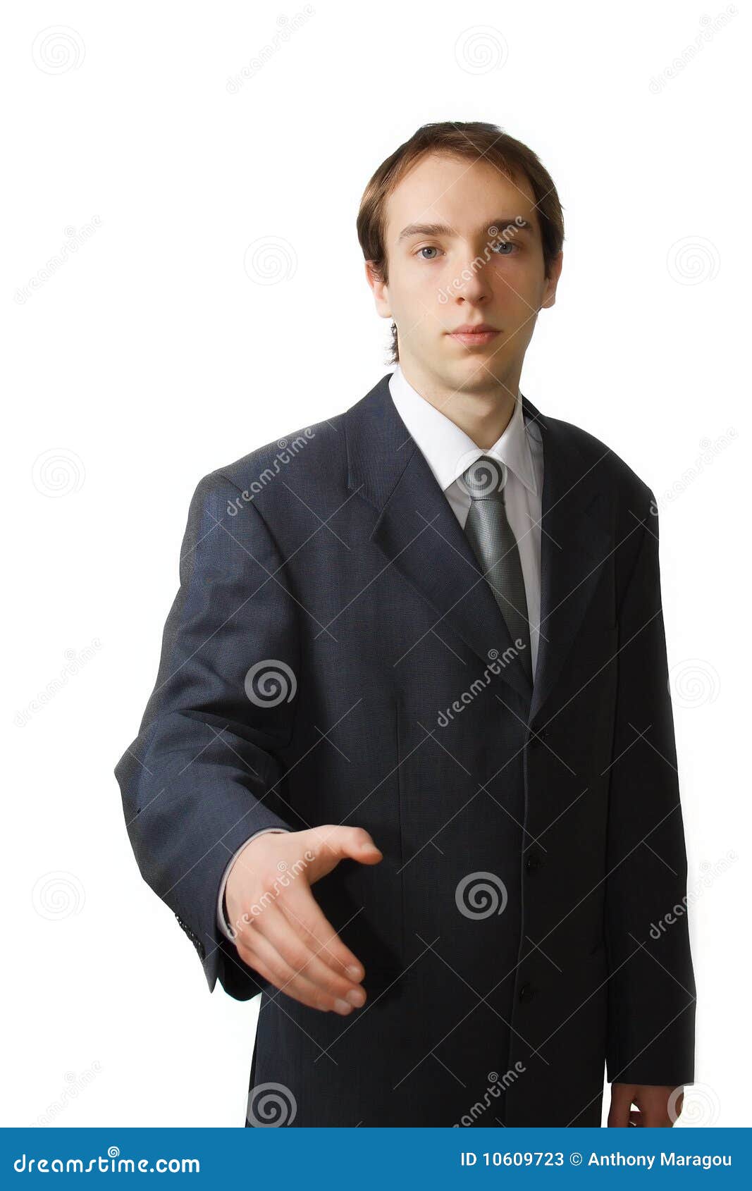 a businessman in a suit and tie extends his hand for a handshake. he is standing against a plain white background.