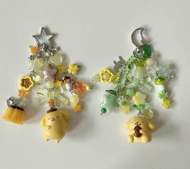 the image shows two pompompurin keychains. the one on the left has a star clip and is decorated with yellow and orange beads and charms. it also has a pudding charm. the one on the right has a moon clip and is decorated with green and yellow beads and charms. it also has a charm of pompompurin holding a chocolate cookie.