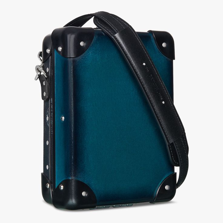 the image shows a blue shoulder bag with black accents and a leather strap. the bag appears to be a small piece of luggage or a travel accessory. the corners are reinforced with black leather and metal studs. a black leather strap is attached to the bag for carrying it over the shoulder.