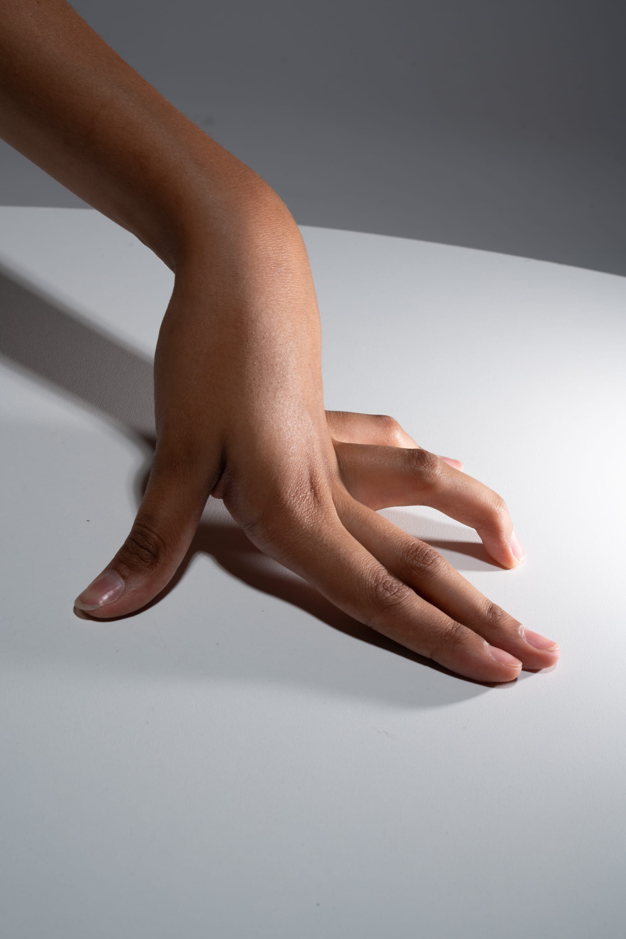 a closeup image of a hand resting on a white surface. the hand is positioned with fingers spread, casting a subtle shadow on the surface. the lighting appears to be artificial, likely studio lighting, creating a soft contrast between the hand and the background.