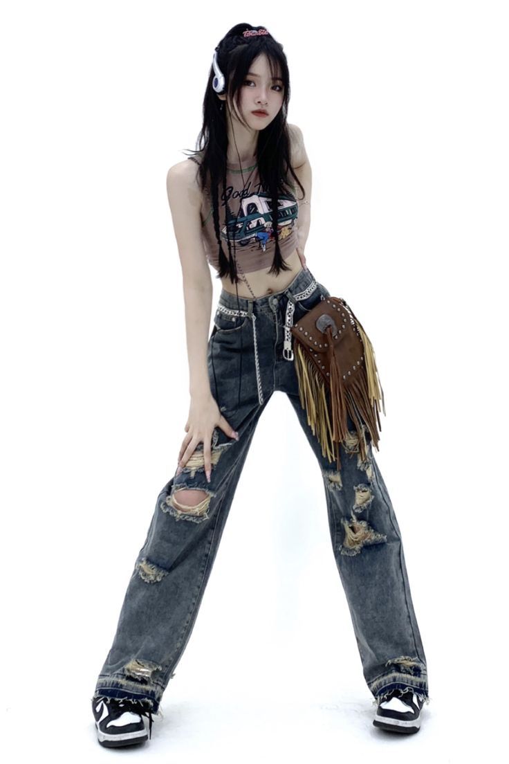a fulllength studio shot of a young woman with long black hair, wearing a graphic tank top, distressed wideleg jeans, a fringed crossbody bag, and sneakers. she is posing against a white background, showcasing her outfit.  her style is a blend of casual and streetwear, incorporating trendy distressed denim and accessories.