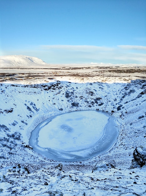 a frozen lake in a snowcovered crater, a landscape with scenic beauty. the blue sky and the white snow contrast nicely against the frozen lake, creating a truly wintery scene. the ice is slightly cracked and the water below is visible. the whole landscape is covered in snow, with the only color being the blue of the sky and the lake.