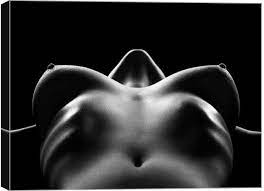 the image is a black and white photograph of a female nude torso.  the subject is positioned lying on their back, with the camera positioned directly above, looking down towards their breasts and abdomen.  the lighting is dramatic, using strong contrasts between light and shadow to highlight the curves and form of the body. the background is entirely black, drawing all attention to the subject's body.  the overall mood is sensual and intimate, yet also artistic and abstract due to the stark lighting and lack of detail in the background.