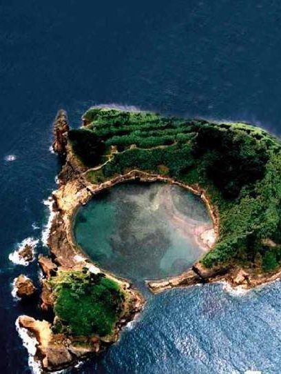 an aerial view of a small, lush green island surrounded by sparkling blue water. the island's interior contains a lagoon of calm, turquoise water. the scene is idyllic, showcasing the beauty of natural landscapes and a sense of tranquility.