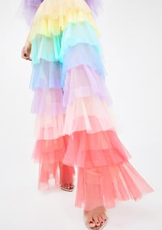 a woman wears a multilayered rainbowcolored tulle skirt with ruffles. the skirt is very full and fluffy, and the colors are bright and vibrant. the woman is wearing sandals with a light background and looks like she is ready for a party.