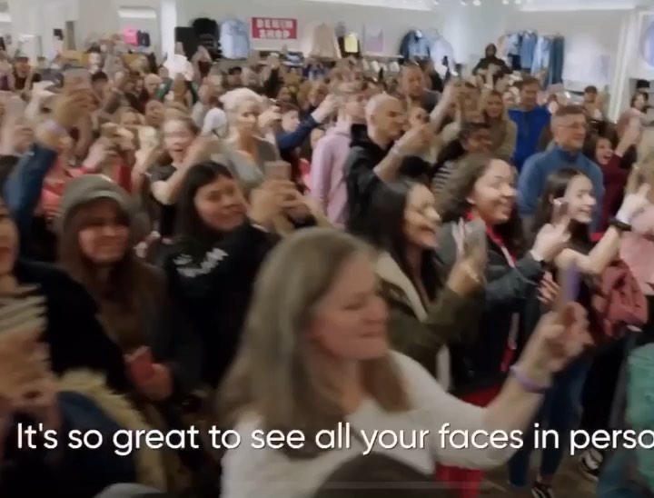 a large crowd of people, seemingly excited, are gathered inside what appears to be a retail store. many are holding up smartphones, taking pictures or recording video. there's a "denim shop" sign visible in the background. the general atmosphere suggests a lively event or gathering, with people smiling and raising their hands. the image is slightly blurred, indicating movement or possibly a quick snapshot. the text at the bottom reads "it's so great to see all your faces in person."