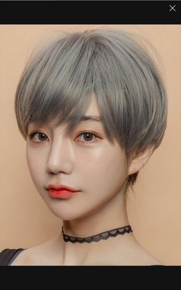 a closeup portrait of an asian woman with short gray hair. she is wearing a black lace choker and looking at the camera.  the background is a plain offwhite color. the woman is looking at the camera.