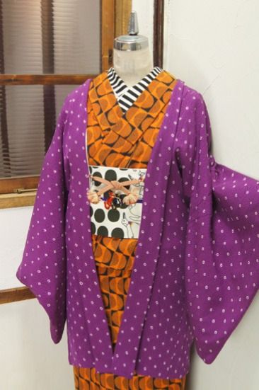 a kimono is displayed on a mannequin. the kimono has a purple polka dot pattern and orange and black shapes in the middle.