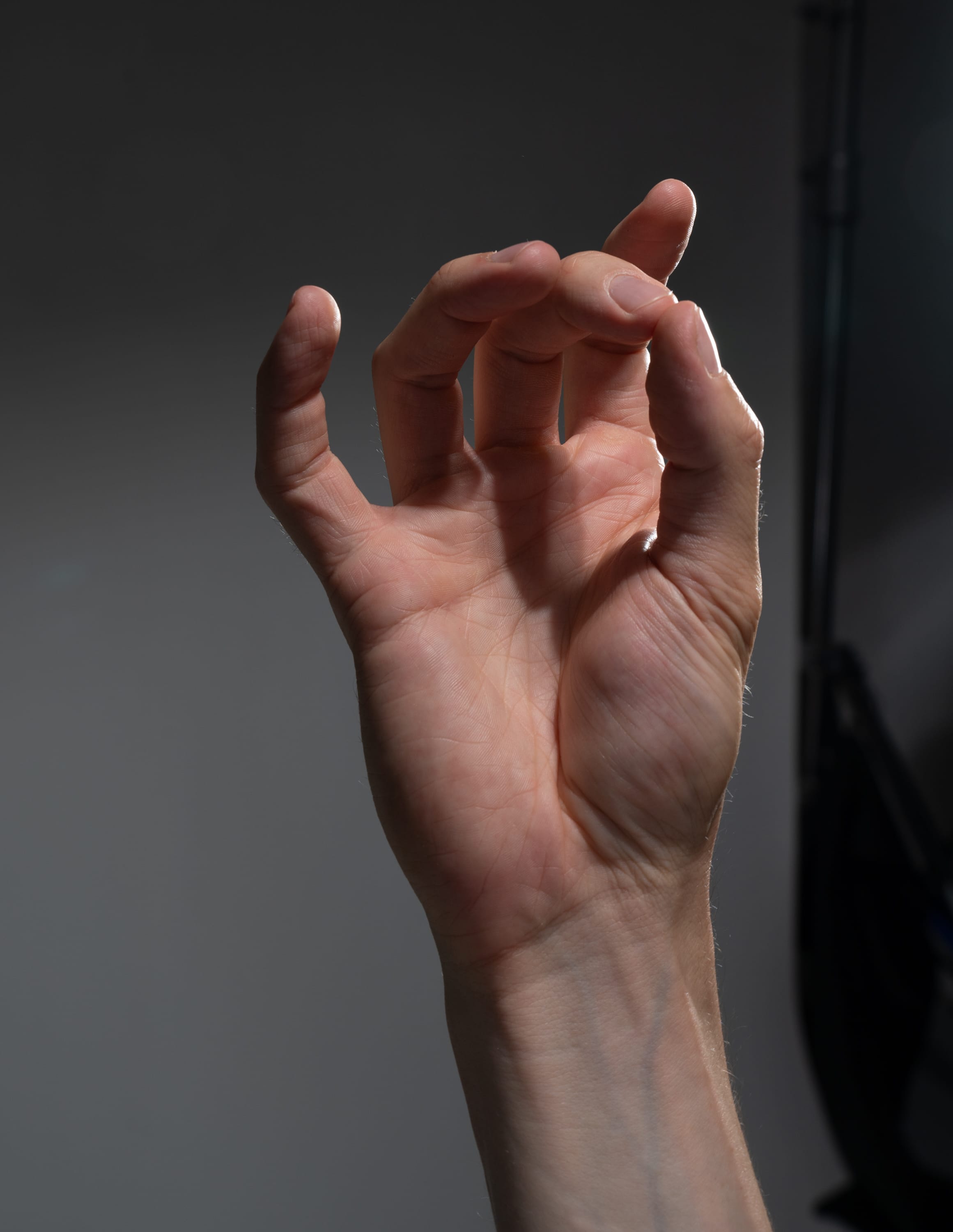 a closeup shot of a person's right hand against a neutral gray background. the hand is slightly contorted, with the fingers curled inward. the lighting is soft and diffused, creating subtle shadows and highlights on the skin.