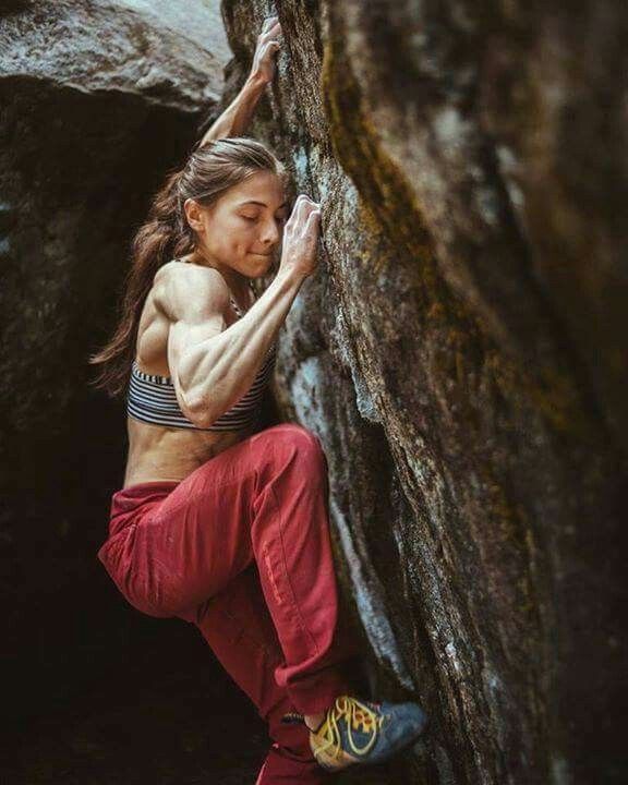 a female rock climber ascends a steep rock face, her body tensed with effort. her muscular arms and determined expression convey the physical and mental demands of the sport. the natural light casts shadows and highlights, emphasizing the textures of the rock and her clothing.