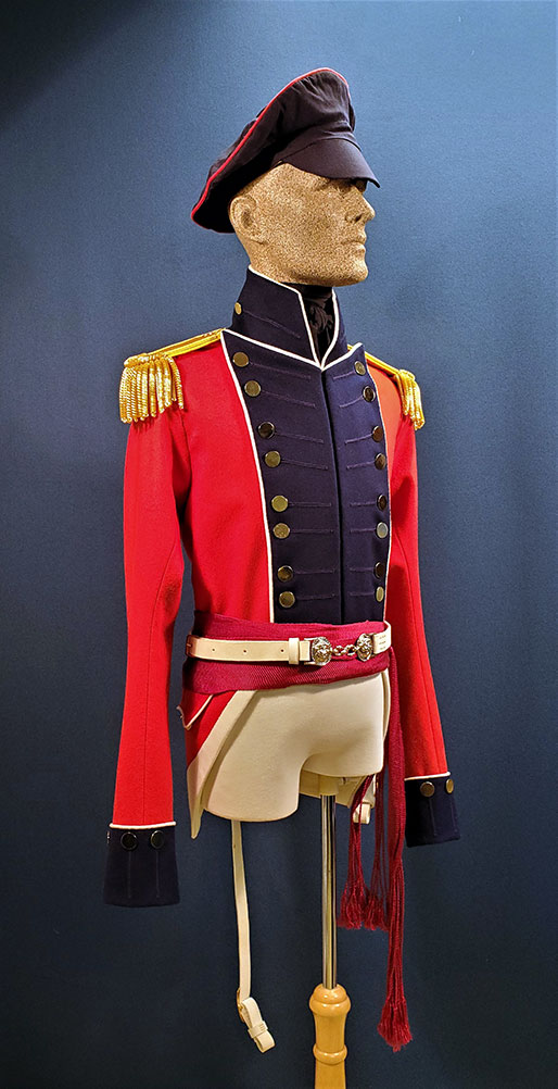a mannequin is wearing a military uniform from the 19th century. the jacket is red with blue lapels and gold trim, and the pants are white. the mannequin is also wearing a white belt and a red sash. the mannequin is wearing a black hat with a red trim. the uniform appears to be inspired by british military uniforms.
