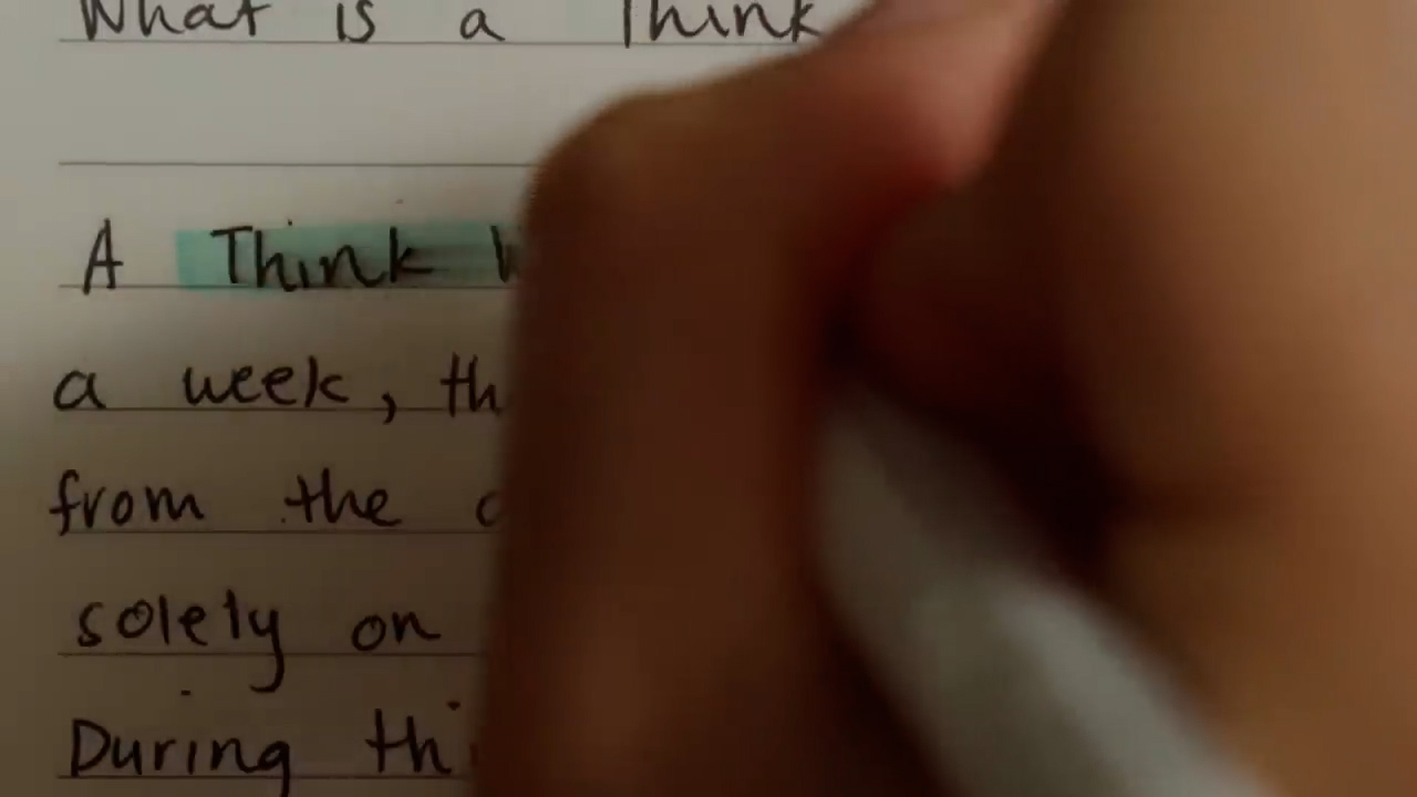 a closeup shot of a person's hand using a highlighter to go over the definition of a "think week." the handwriting on the notepad is clear, suggesting a thoughtful and deliberate approach to defining this term.