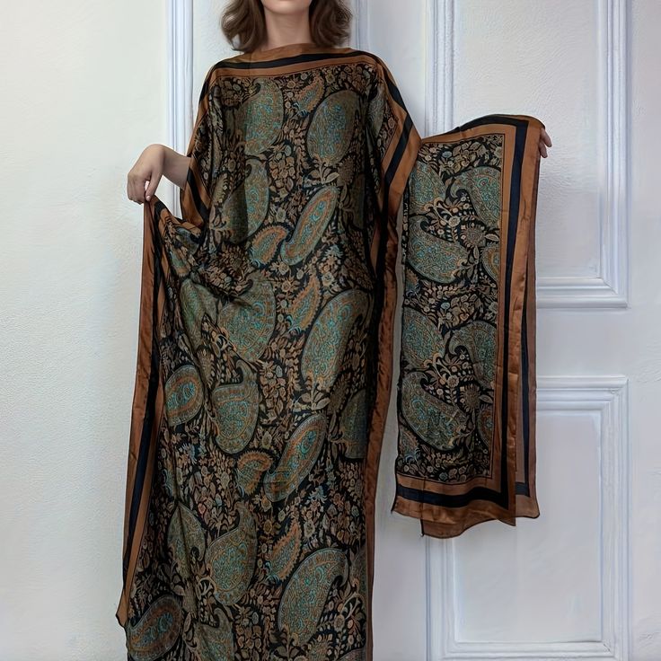a woman is modeling a long, flowing silk dress with a paisley print. the dress is predominantly dark brown and black with teal and gold paisley patterns. it has wide sleeves and a relaxed fit, resembling a kaftan or kimono style. the model is standing against a white background. the dress is shown in detail, highlighting the fabric's texture and print.