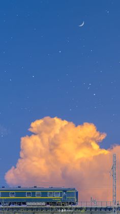 a green train is moving along a bridge from left to right with a giant sunsetlit cloud behind it that takes up the majority of the image space. the sky above the cloud is a dark blue with a scattering of stars and a crescent moon on the upper right. the overall impression is one of peace and serenity.