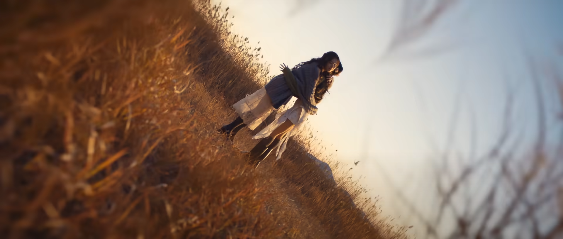 two women embrace in a field of tall, golden grass. the sun is setting, casting a warm, golden light on the scene. the perspective is from a low angle, emphasizing the height of the grass and the intimacy of the hug. the overall feeling of the image is one of warmth, love, and connection.