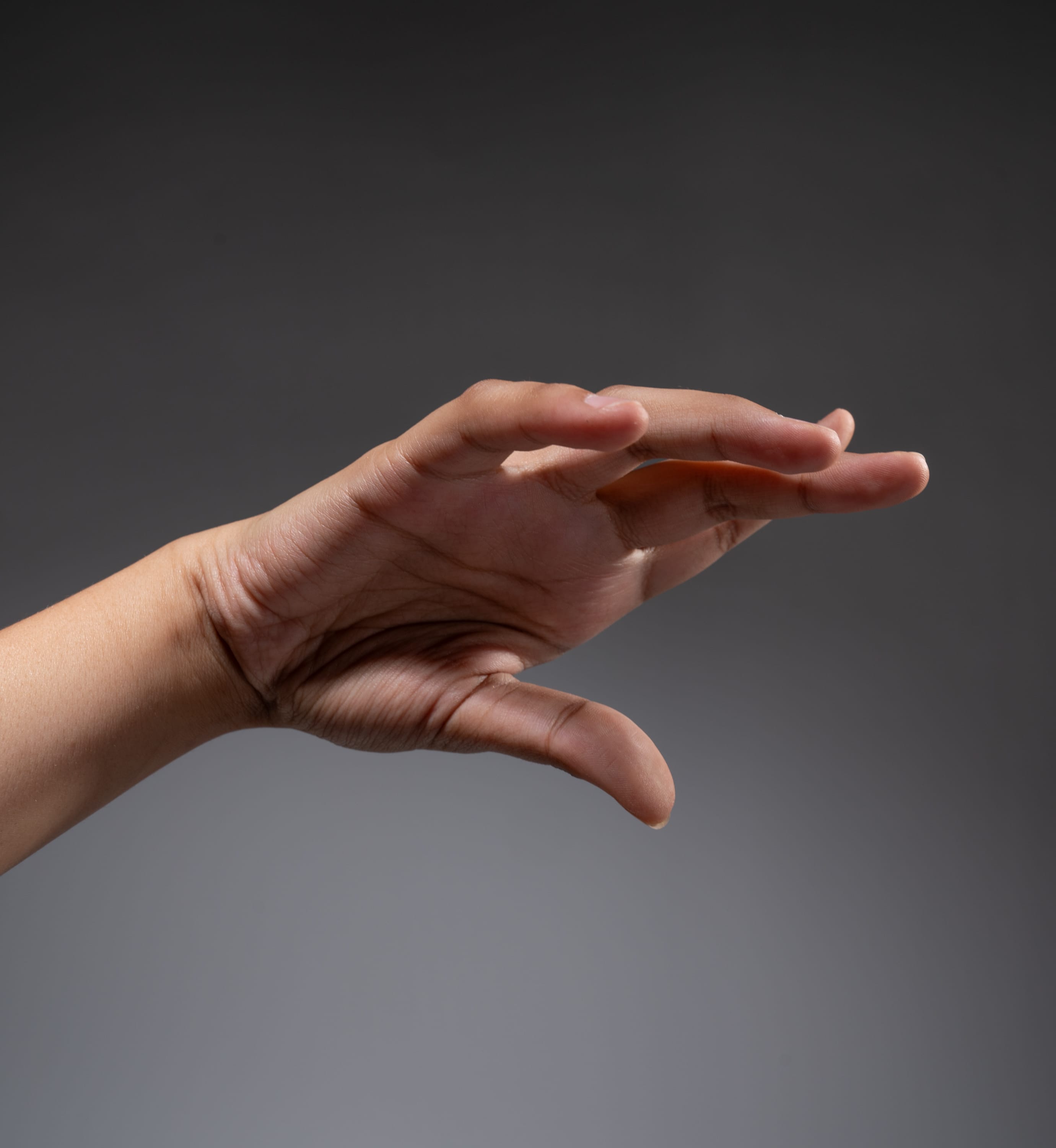 a hand is reaching out with its fingers slightly curled, as if about to grab something. the hand is illuminated by studio lighting against a neutral gray background, highlighting the details of the skin and the gesture.