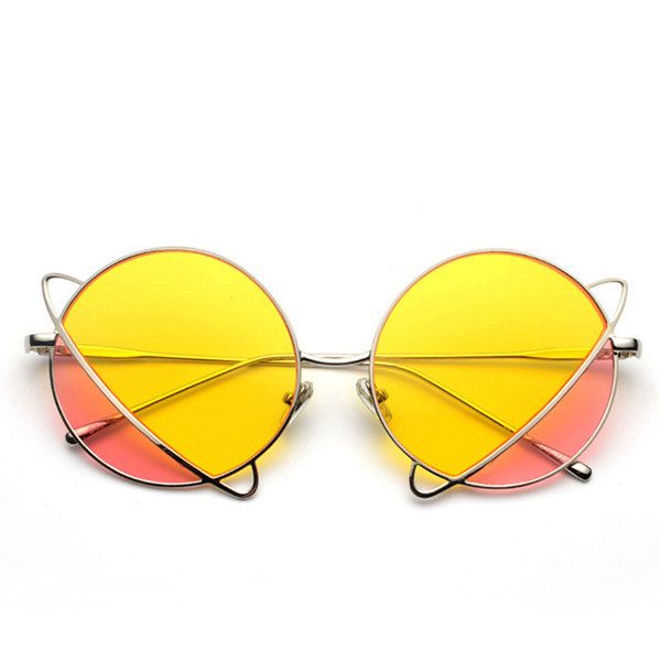 a closeup studio shot of a pair of round sunglasses with yellow lenses that fade to a pink tint on the bottom. the frames are silver, and the glasses feature a unique design with additional metal accents that curve around the lenses at the top and bottom, resembling cat ears.