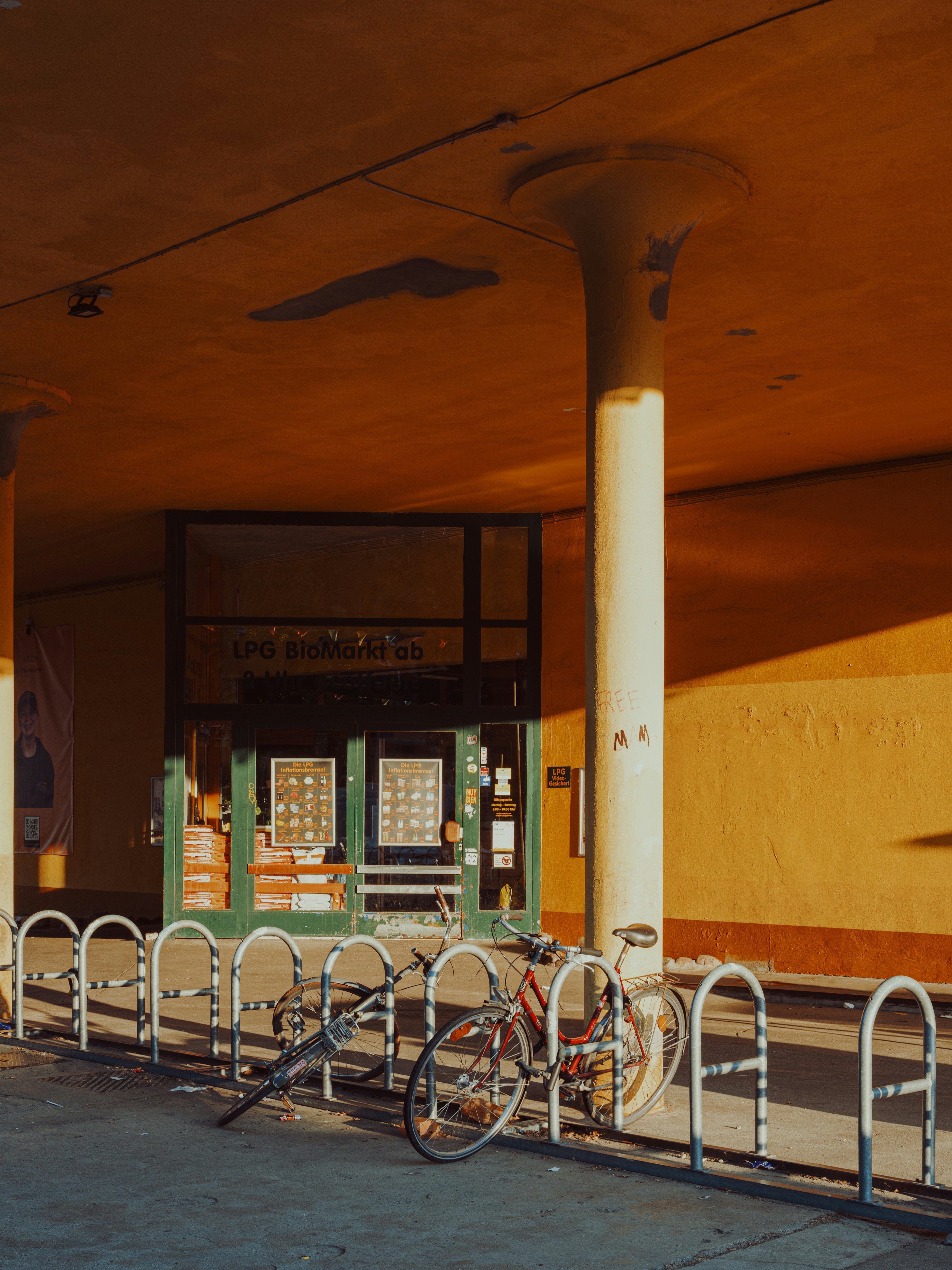 a bicycle leans against a metal railing in front of a closed shop. the building is bathed in the warm, golden light of the late afternoon sun, creating long shadows across the sidewalk. the shopfront has a vintage feel with multiple windows showcasing its wares.  the overall mood is peaceful and somewhat nostalgic.