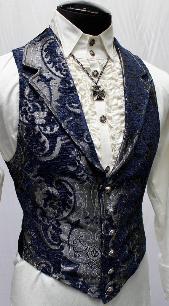 a closeup shot of a men's fashion outfit. the outfit features a navy blue paisley vest with silver buttons, a white dress shirt with ruffles, and a silver cross pendant necklace. the vest is buttoned up.