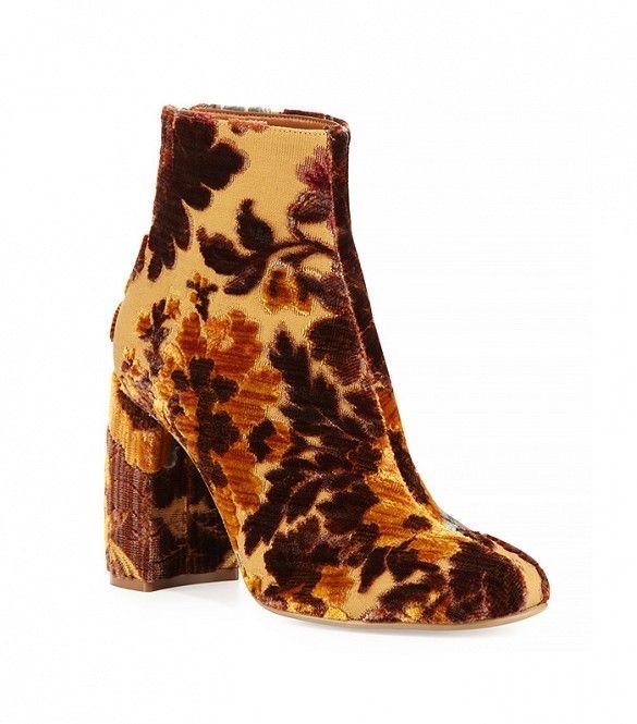 a closeup shot of a single floral velvet ankle boot with a high block heel. the boot features a mix of brown and beige tones in a floral pattern. the design is bold and intricate, covering the entire surface of the boot. the sole and interior lining are visible. the boot is positioned on a white background, which accentuates its colors and design.