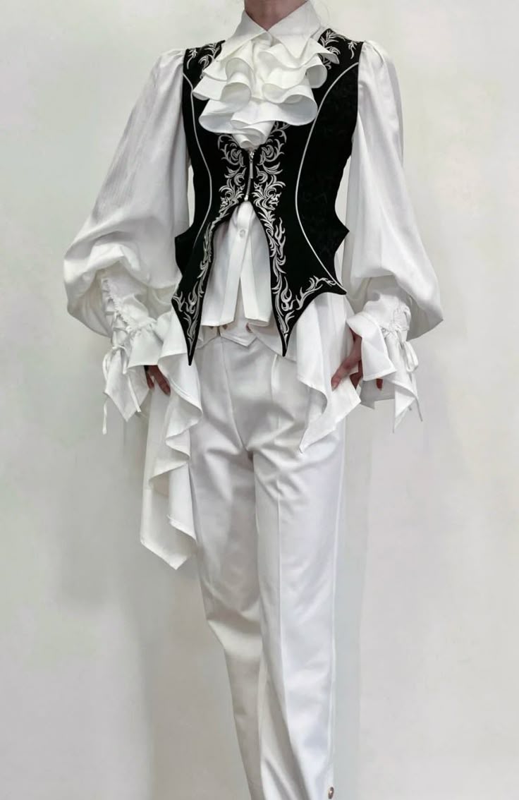 a person is dressed in an elaborate white suit with a black vest over the shirt. the shirt has ruffles. the vest is embroidered with a swirling pattern. the background is white.