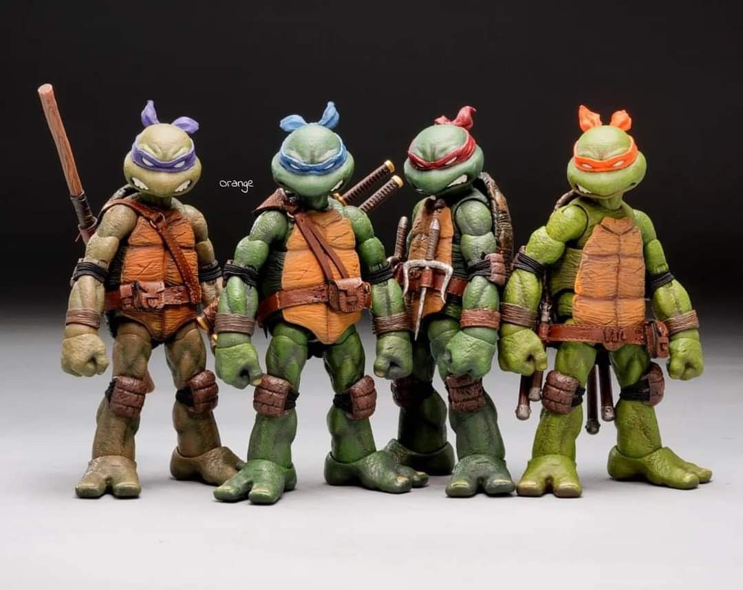 the image shows four teenage mutant ninja turtles action figures standing sidebyside. from left to right, the turtles are donatello (purple mask, bo staff), leonardo (blue mask, katana swords), raphael (red mask, sai), and michelangelo (orange mask, nunchucks). the figures are detailed and appear to be highquality collectibles. they are standing against a dark background with a lightcolored surface beneath them.