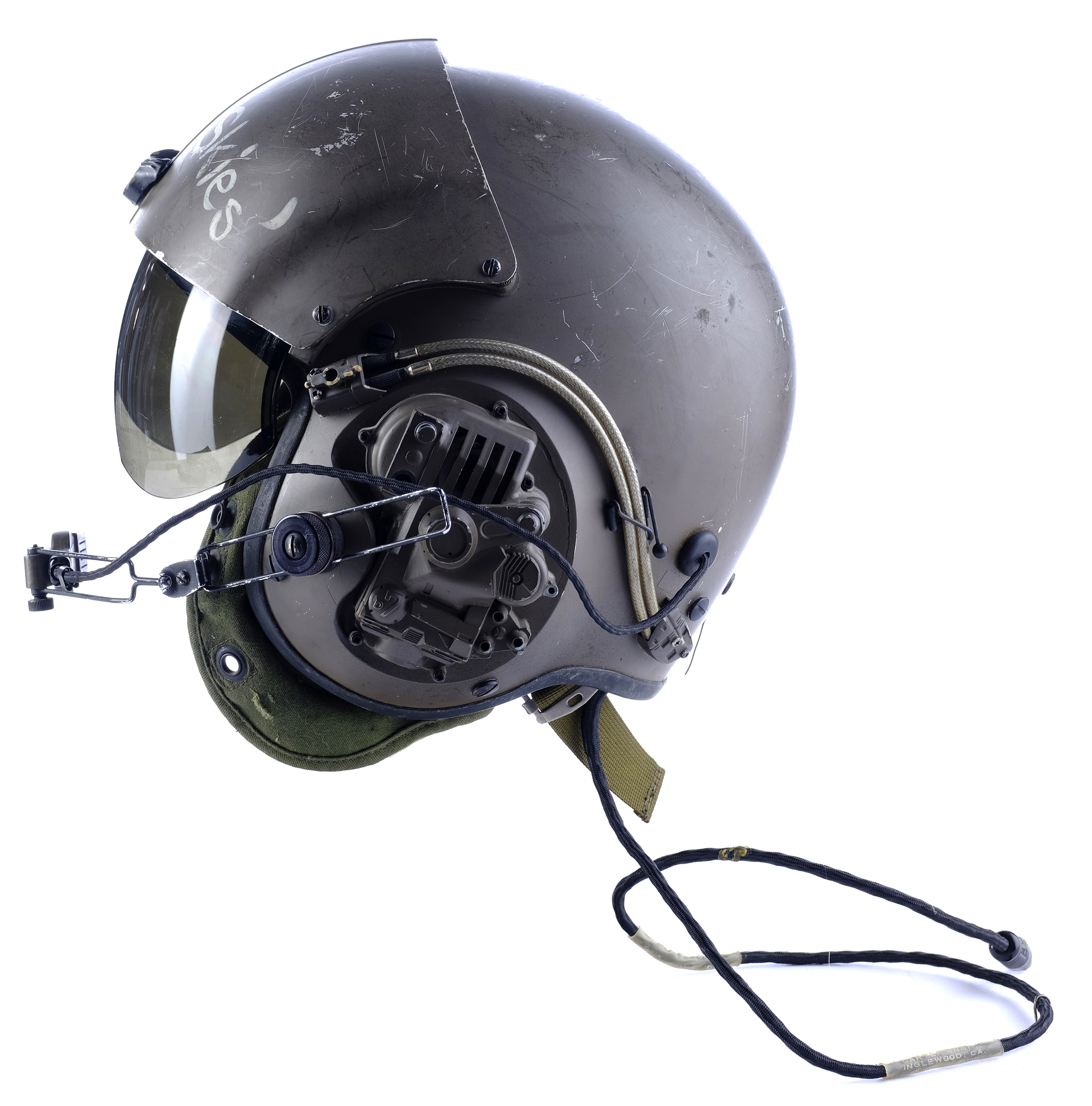 a closeup view of a military aviator helmet, showing the side with the visor down, the communication cord attached, and some other equipment, like a microphone. the helmet has the word "wiles" inscribed on the side.  it appears to be a wellworn helmet.  the helmet is a deep brown color with some green and black details.