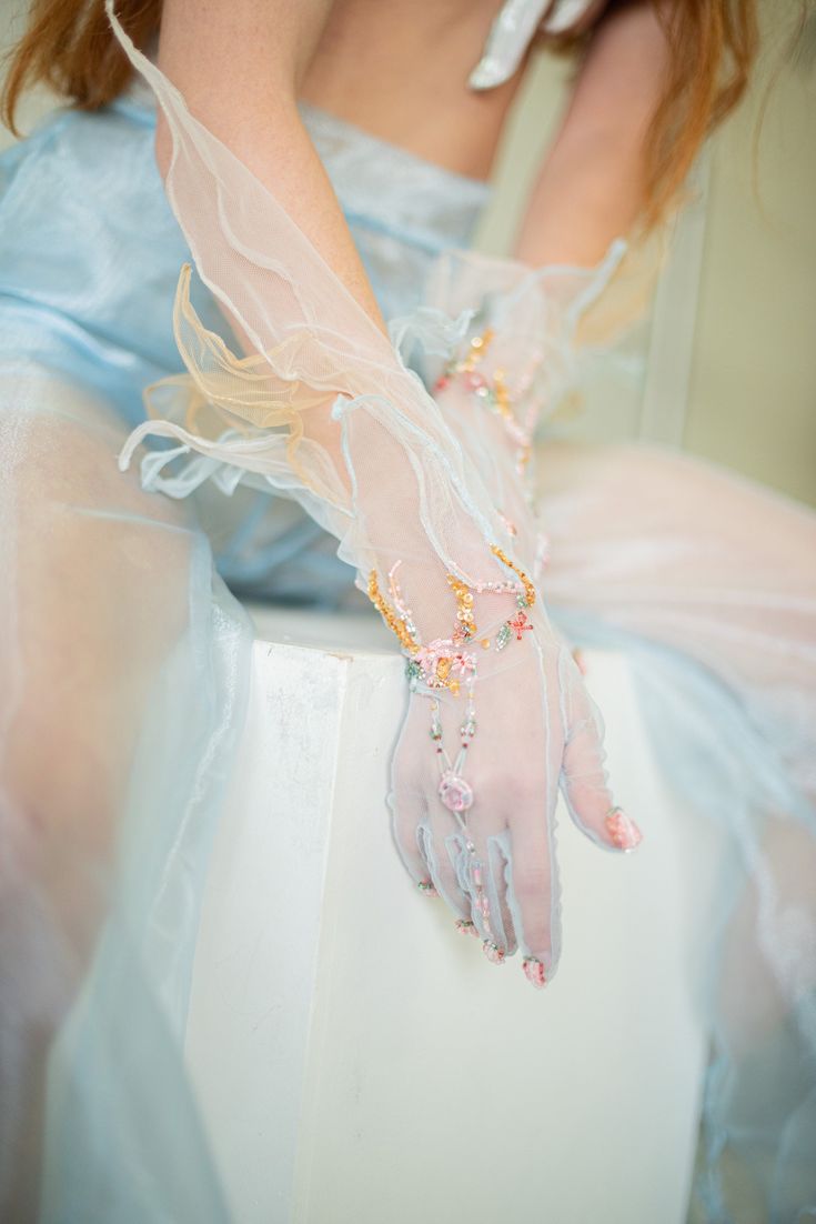 a woman wearing a white gown with lace detailing sits with her hand adorned with a delicate lace glove and jewelry. the image captures a sense of elegance and romanticism.
