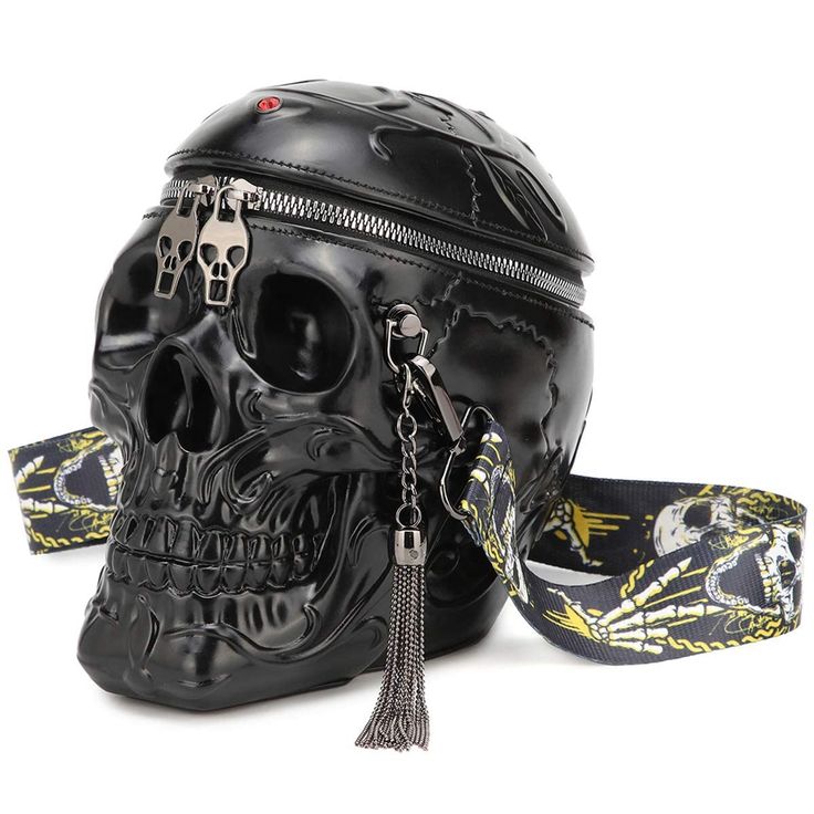 a black, shiny, skullshaped purse with a zipper along the top, adorned with skull zipper pulls. the purse also features a black strap printed with skeleton hands and skulls, and a metal tassel hanging from the side.